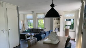 A modern living room with a wooden dining table, blue chairs, a grey sofa, and a black pendant light.