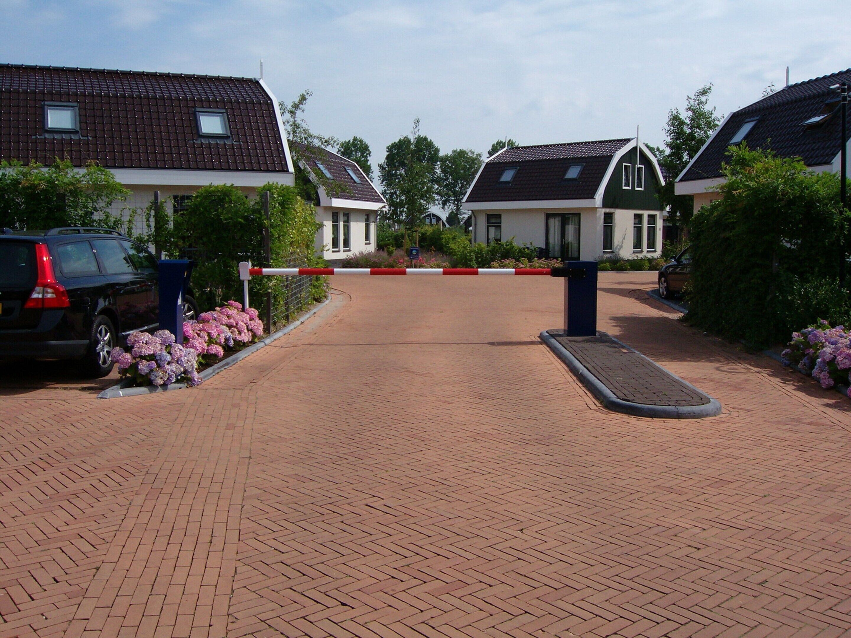 Een hek afsluit een oprit die leidt naar een rij huizen met een tegelpad.