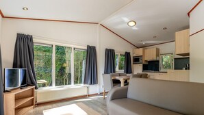 A modern living room with a sofa, a TV, and a dining area with a table and chairs. - Family Chalet in Netherlands Holiday Park (Egmond aan den Hoef)