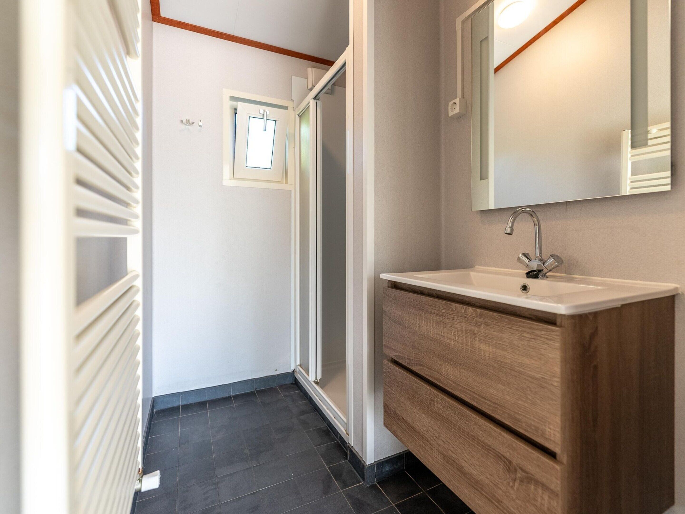 Un baño moderno con un lavamanos blanco, tocador de madera y un espejo sobre el lavamanos.