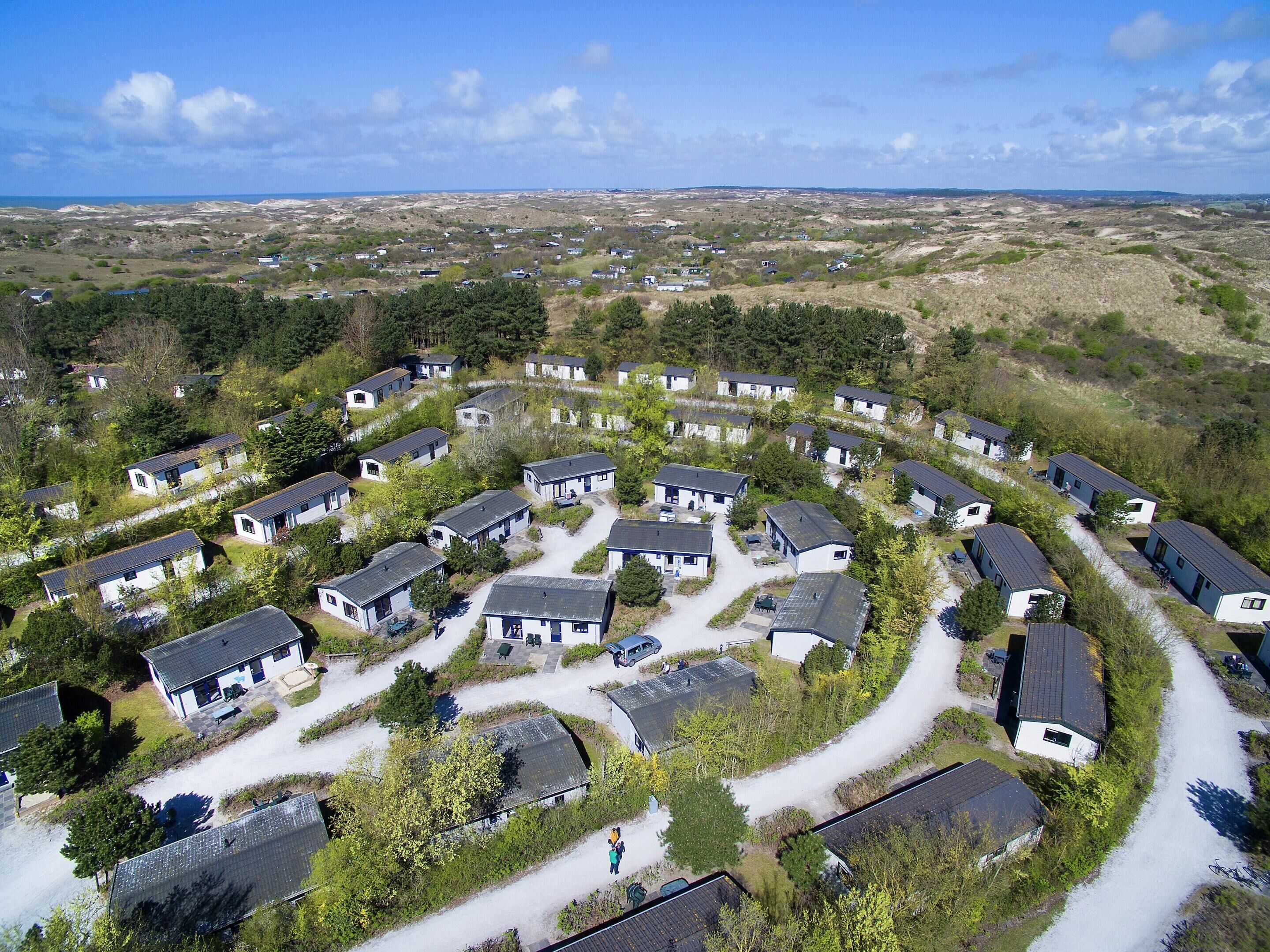 A circular layout of cottages with a gravel path connecting them, surrounded by greenery and a distant view of the sea.