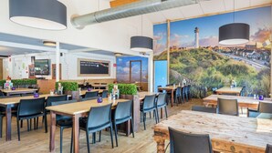 A restaurant with wooden tables and chairs, a large mural of a coastal scene, and a chalkboard sign. - Family Chalet in Netherlands Holiday Park (Egmond aan den Hoef)