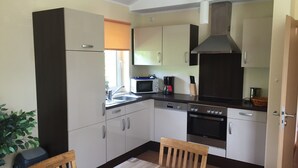 A compact kitchen with white cabinets, a microwave, a coffee maker, and a stove. - Bungalow in Eifel Near Mountain Trails (Gerolstein)
