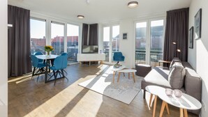 Een moderne woonkamer met een eethoek, grote ramen en een bank.