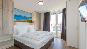 Een moderne slaapkamer met een bed, een schilderij, een televisie en een balkon met gordijnen.