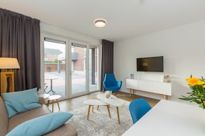 Un salon moderne comprenant un canapé, des fauteuils, une table basse, un téléviseur et une porte-fenêtre coulissante donnant sur un espace extérieur.