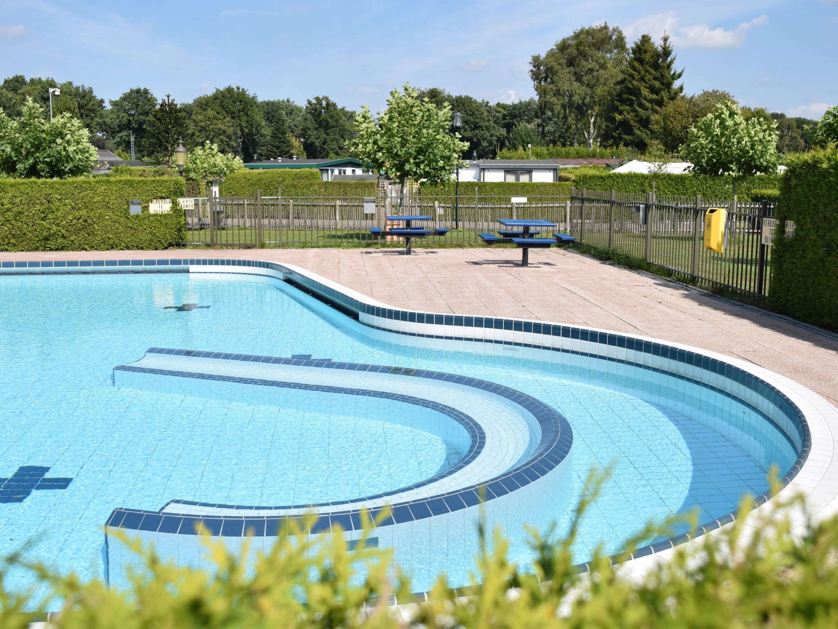 A swimming pool with a curved design, surrounded by a fence and benches.