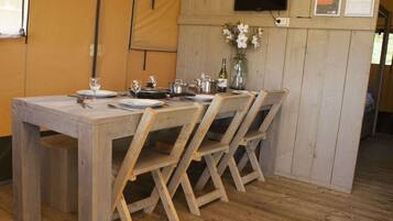 A wooden dining table with four chairs, a TV mounted on the wall, and a small vase with flowers.