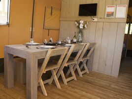 A wooden dining table with four chairs, a TV mounted on the wall, and a small vase with flowers.