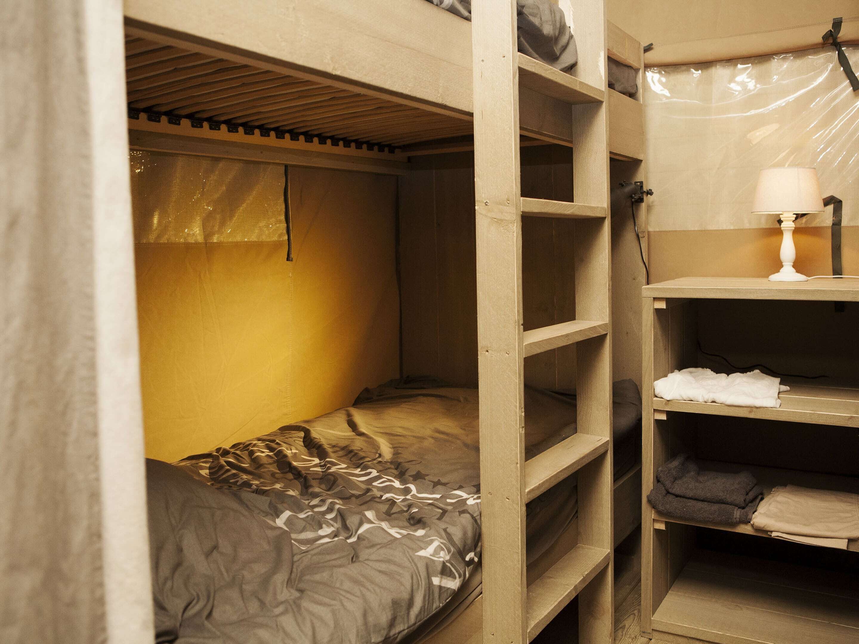 A bunk bed with a headboard, a bedside table with a lamp, and a shelf with folded clothes.