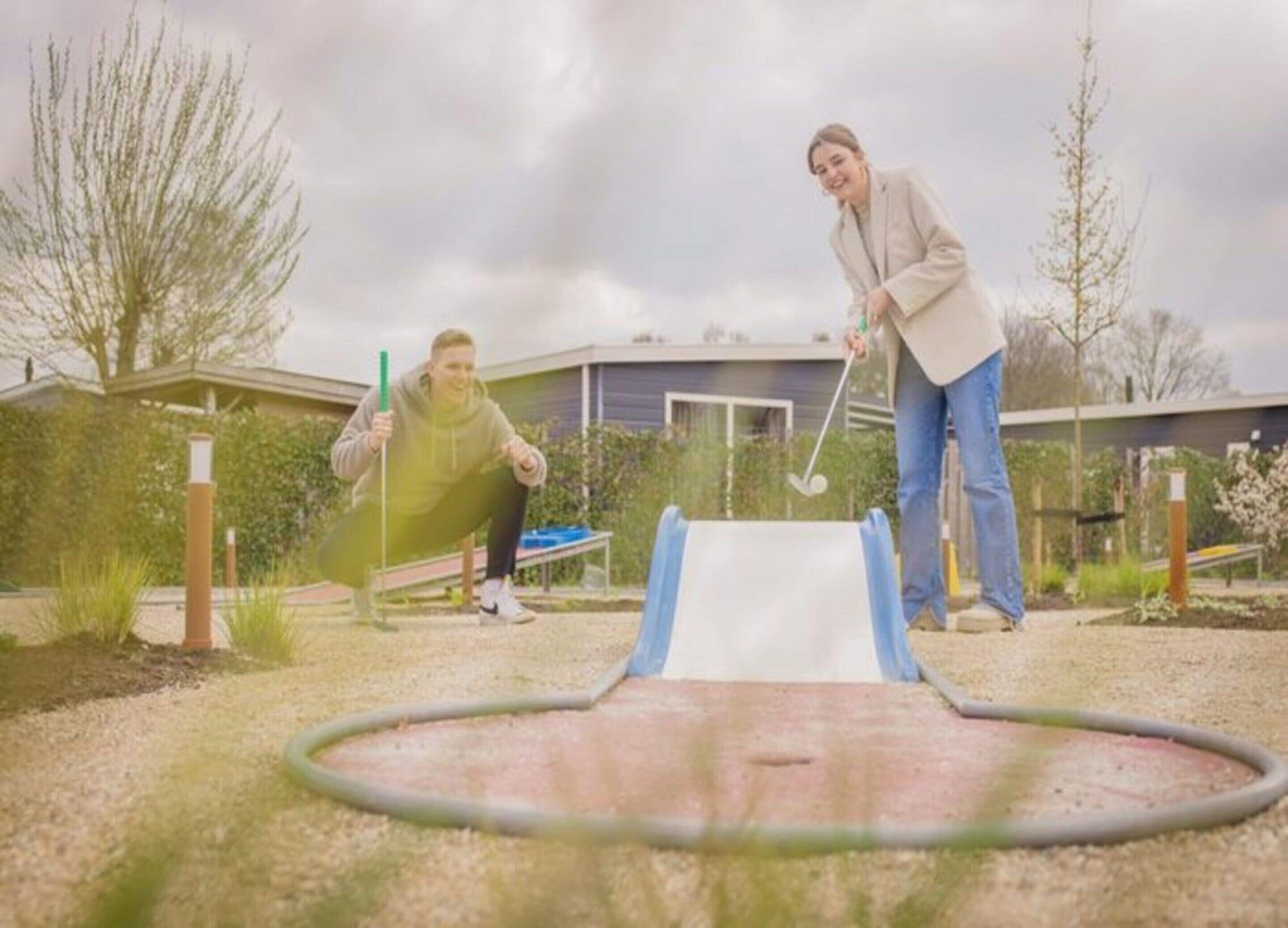 Deux personnes jouant au golf dans un jardin, avec un green d’entraînement et une maison en arrière-plan.