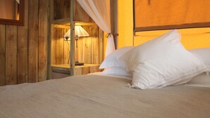 A wooden room with a bed, a nightstand, a lamp, and a window with curtains. - Comfortably Furnished Tent Lodge with Stove near Veluwe (Voorthuizen)