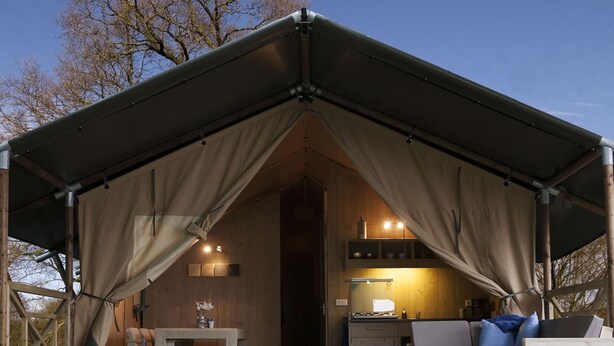 A cozy, enclosed outdoor space with a wooden table, a bench, and a sofa under a large, dark-colored canopy. - Comfortably Furnished Tent Lodge with Stove near Veluwe (Voorthuizen)