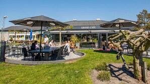 An outdoor seating area with tables and umbrellas at a restaurant named GRAND-CAFE. - Modern Chalet With Dishwasher in Noordwijk Near the Sea (Noordwijk)