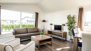 A modern living room with a sofa, coffee table, TV stand, and a dining area. - Modern Chalet With Dishwasher in Noordwijk Near the Sea (Noordwijk)