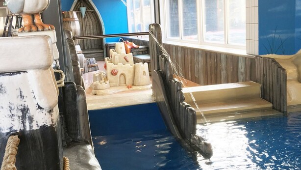 An indoor pool with a castle-themed water slide, a seagull statue, and a blue wall. - Modern Chalet With Dishwasher in Noordwijk Near the Sea (Noordwijk)