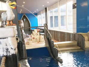 Una piscina interior con un tobogán de agua con temática de castillo, una estatua de gaviota y una pared azul.