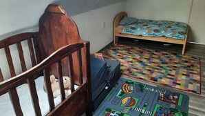 A small, cozy room with a wooden crib, a single bed with a colorful bedspread, and a play mat on the floor. - Holiday Home in Quiet Environment near Beach & Dunes (Groet)