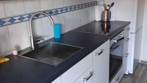 A modern kitchen with a black countertop, stainless steel sink, and white cabinets. - Holiday Home in Quiet Environment near Beach & Dunes (Groet)