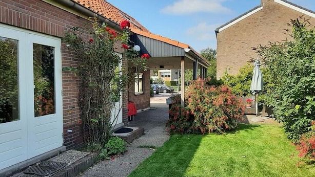 A residential property with a brick house, a covered porch, and a well-maintained garden. - Holiday Home in Quiet Environment near Beach & Dunes (Groet)
