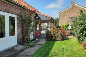 A residential property with a brick house, a covered porch, and a well-maintained garden. - Holiday Home in Quiet Environment near Beach & Dunes (Groet)