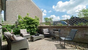 A patio area with wicker furniture, a table, and a chair. - Holiday Home in Quiet Environment near Beach & Dunes (Groet)