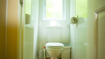 A small, narrow bathroom with a toilet, a radiator, a window, and a trash bin.