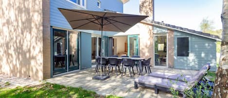 A modern house with a patio area featuring a table and chairs, an umbrella, and a lounge chair.
