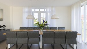 A modern dining area with a wooden table, grey upholstered chairs, and a vase of flowers. - Villa in Cadzand-bad Near North Sea Coast (Cadzand-Bad)
