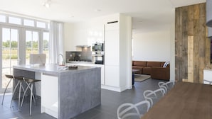 A modern kitchen with a central island, a dining area with a wooden table, and a living space with a sofa. - Villa in Cadzand-bad Near North Sea Coast (Cadzand-Bad)