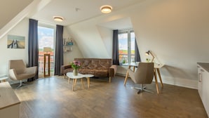 Un loft moderno con techo inclinado, un sofá de cuero marrón, una mesa de centro blanca y un área de comedor con una mesa y sillas blancas.