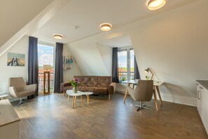 A modern loft apartment with a sloped ceiling, a brown leather sofa, a white coffee table, and a dining area with a white table and chairs. - Terrace Flat in Zoutelande (Zoutelande)