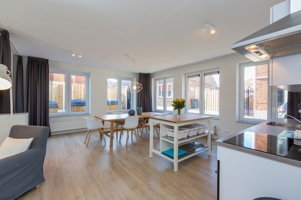 A modern kitchen with a dining area, large windows, and a sofa.