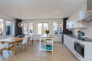A modern kitchen with white cabinets, a wooden dining table, and a view of the street.