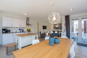 A modern kitchen with white cabinets, a wooden dining table, and a geometric pendant light. - Terrace Flat in Zoutelande (Zoutelande)
