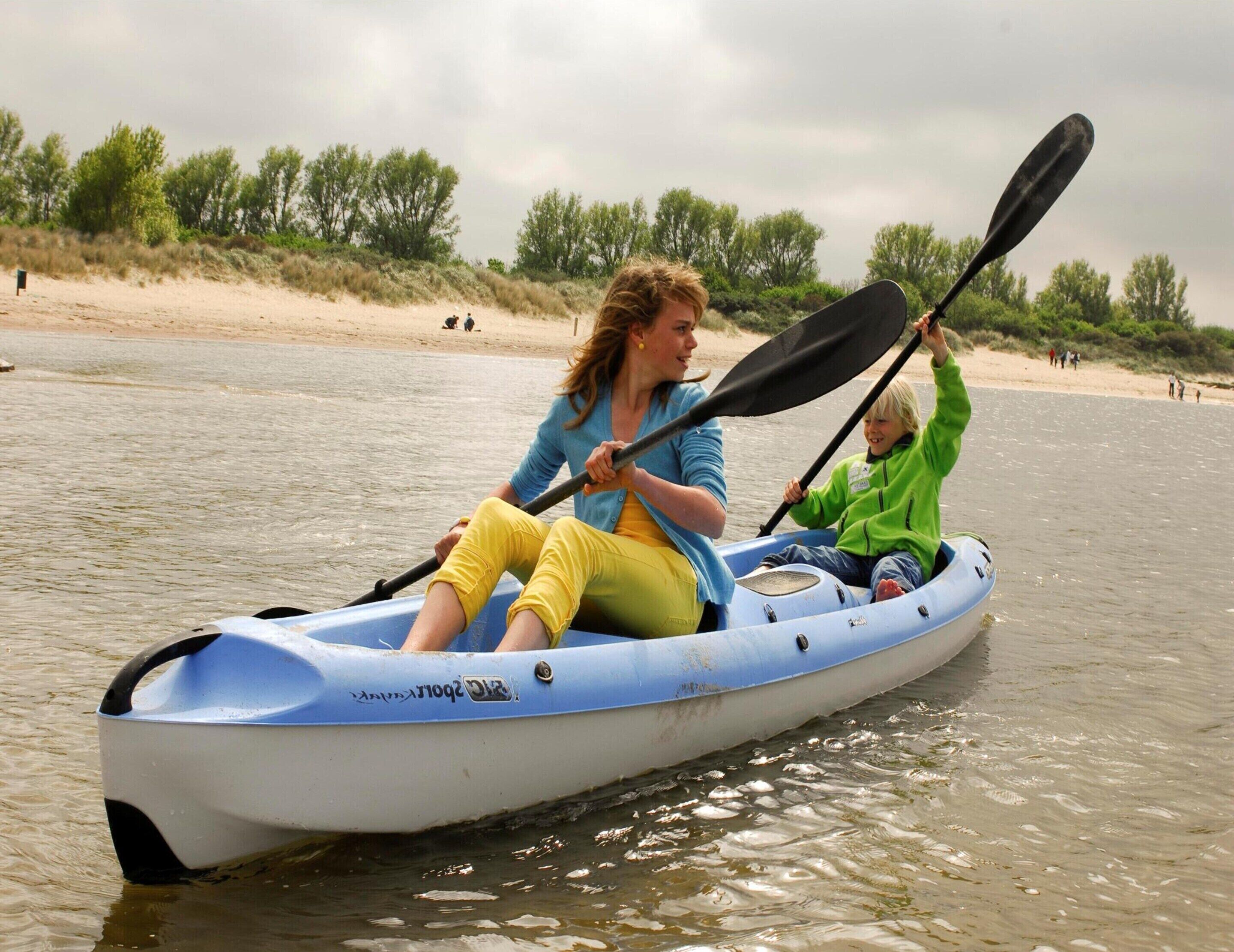 A kayak on a river with a sandy beach and trees in the background.