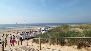 A beachside walkway leading to a beach area with a lifeguard tower and a boat dock. - Cozy Apartment near Sea in Bergen aan Zee (Bergen aan Zee)