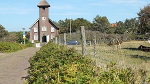 A brick church with a bell tower, a paved path, and a fenced area with a car and a cow. - Cozy Apartment near Sea in Bergen aan Zee (Bergen aan Zee)