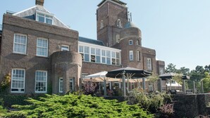 A large brick building with multiple windows and a tower. There are outdoor umbrellas and seating areas. - Cozy Apartment near Sea in Bergen aan Zee (Bergen aan Zee)