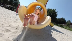 Un enfant sur un toboggan jaune dans un terrain de jeu sablonneux.