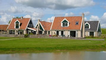 A row of traditional houses with pitched roofs and chimneys, a grassy area in front, and a body of water.