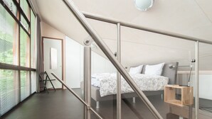 Ein modernes Schlafzimmer mit einer Glasstiege, einem Bett mit weißer Bettwäsche und Blick ins Freie durch große Fenster.