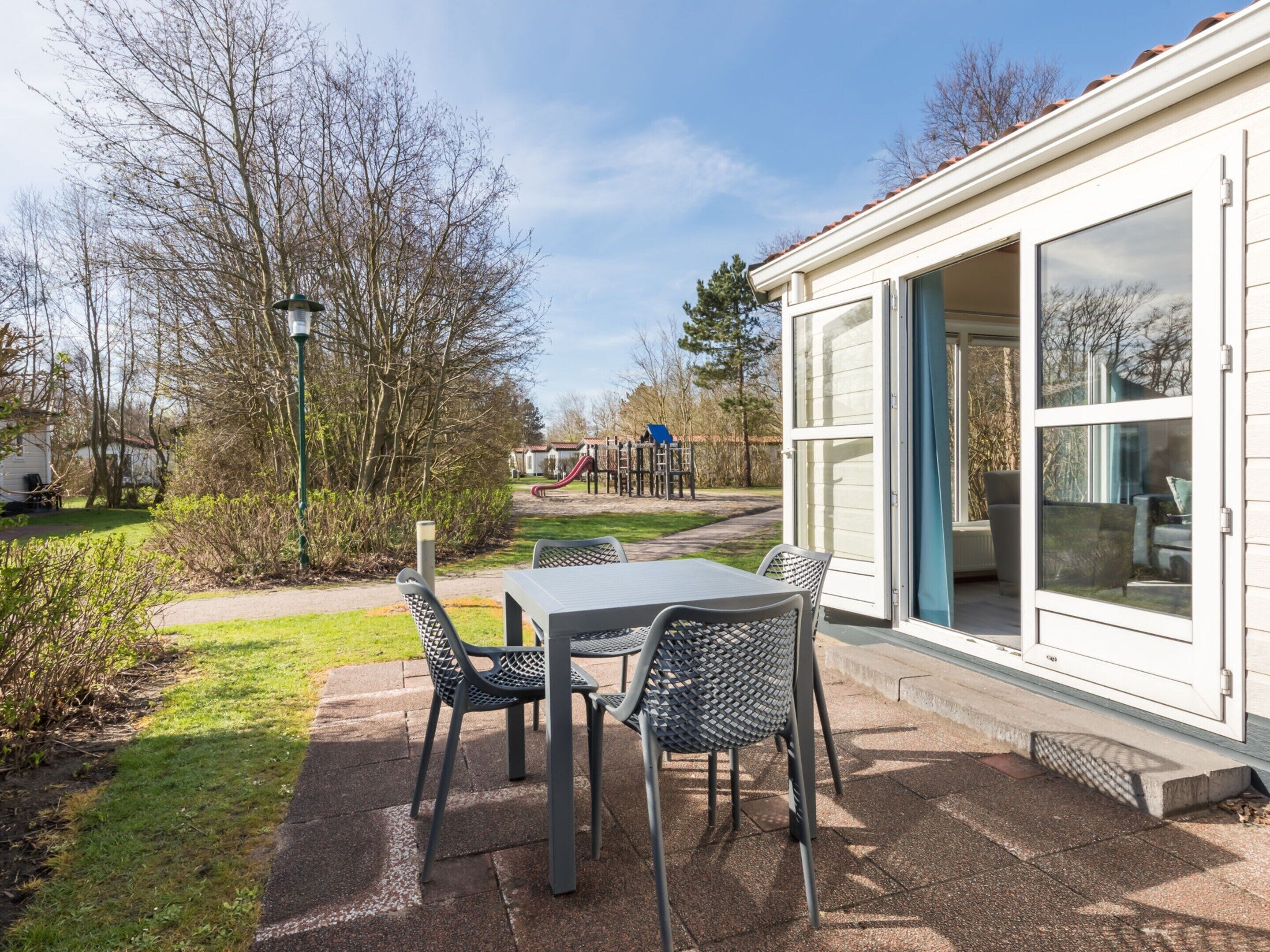 Eine Terrasse mit Tisch und Stühlen, im Hintergrund ein Spielbereich und ein Gebäude mit großen Fenstern.