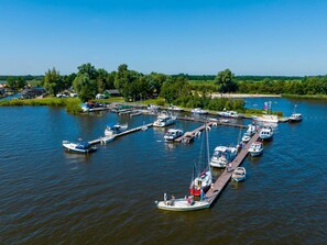 A marina with multiple boats docked at piers, surrounded by greenery and a clear sky.