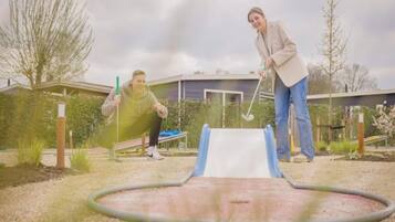 Two people playing golf in a backyard with a putting green and a house in the background.