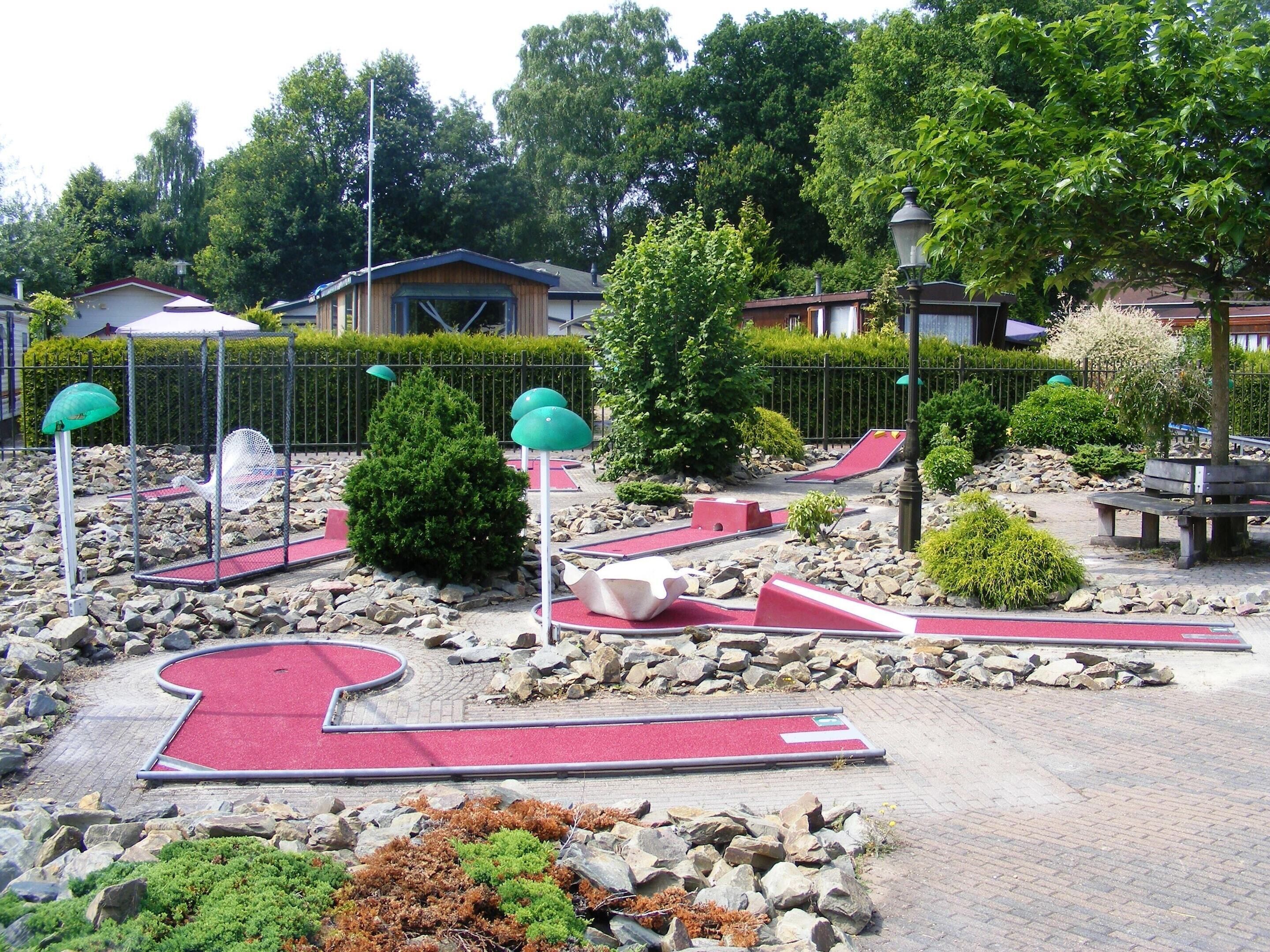Un parcours de minigolf doté d’une surface de jeu rouge, entouré de rochers et de verdure.