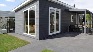 A modern house with large sliding glass doors, a patio with outdoor furniture, and a covered area with tables and chairs. - Atmospheric Chalet with Porch near Veluwe (Voorthuizen)