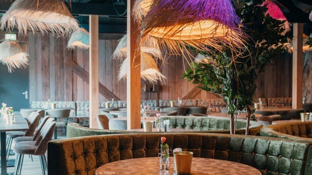 A restaurant with round tables and cushioned booths, featuring thatched umbrellas and wooden walls. - Atmospheric Chalet with Porch near Veluwe (Voorthuizen)