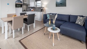 A modern living room with a blue sofa, a dining table with chairs, a kitchen area, and a small side table with a vase. - Cozy Chalet Near Breskens Sea (Breskens)