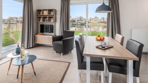 A modern living room with a dining table, chairs, a TV, and a view of a residential area. - Cozy Chalet Near Breskens Sea (Breskens)